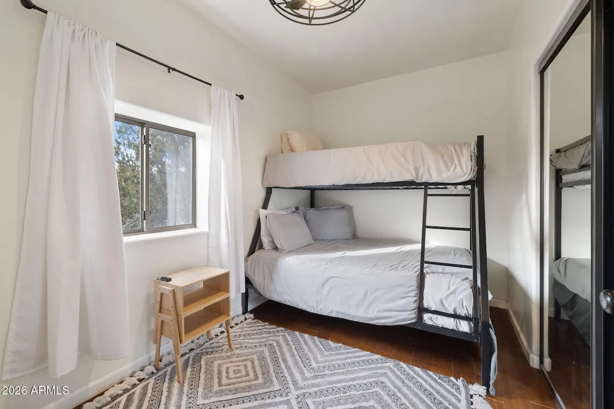 The bunk room: a black metal bunk bed with white bedding beside a window, and mirrored closet doors reflecting the room.